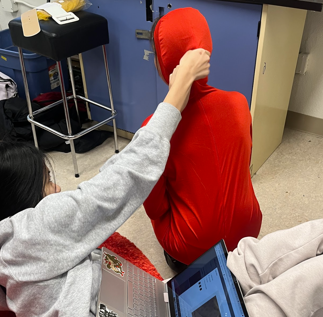 Celia zipping up Audrey's red suit