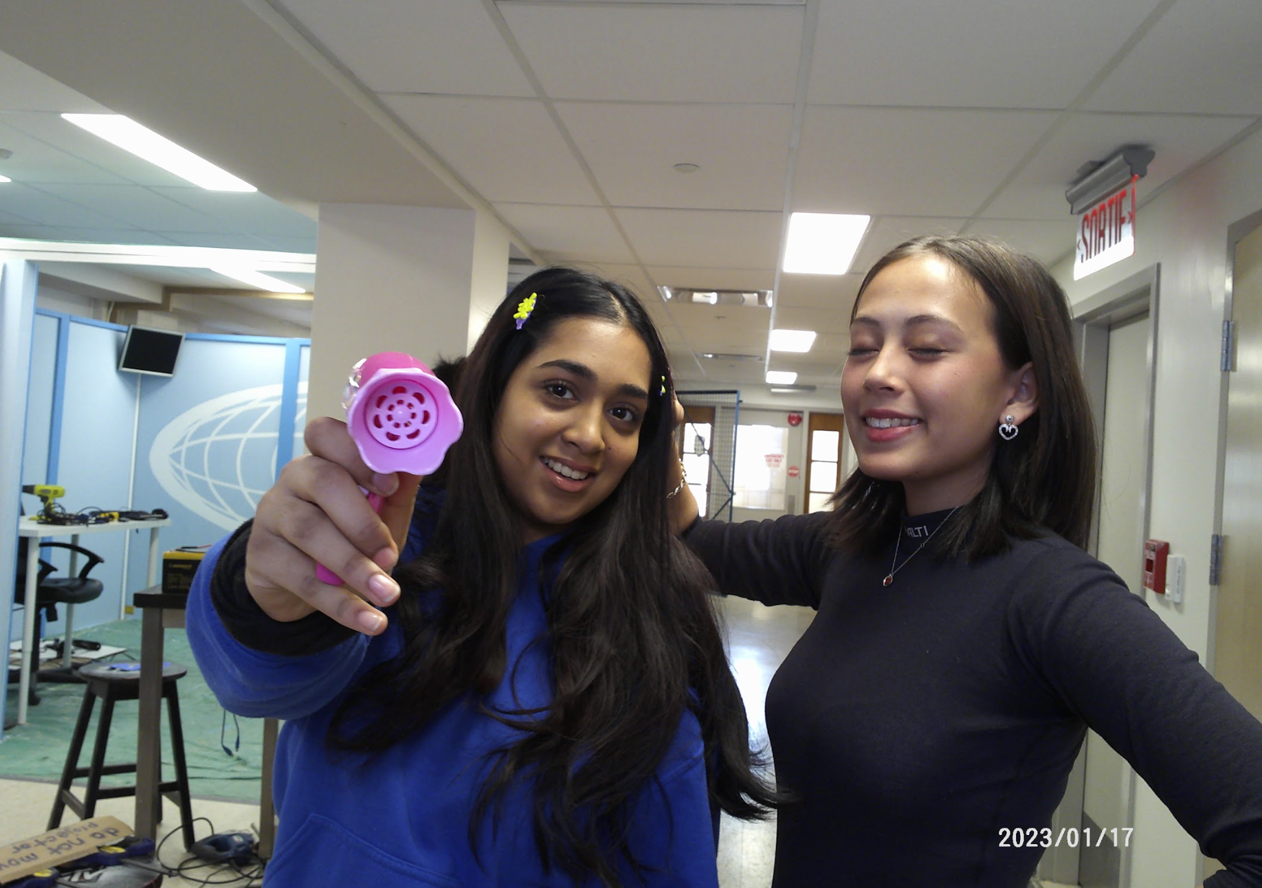 Nehna pointing a pink toy blowdryer to the camera with Audrey