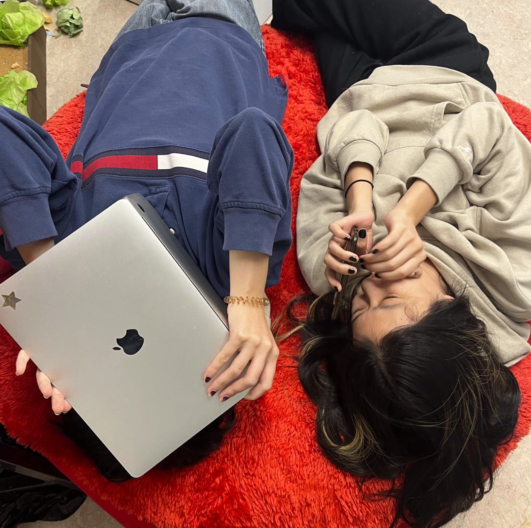 Victoria hiding behind her laptop, Celia next to her on a red couch